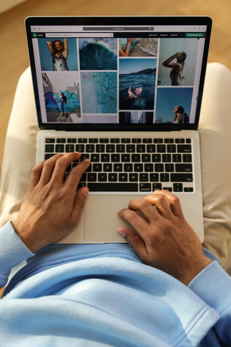 Close-up of hands typing on a laptop displaying travel photos.